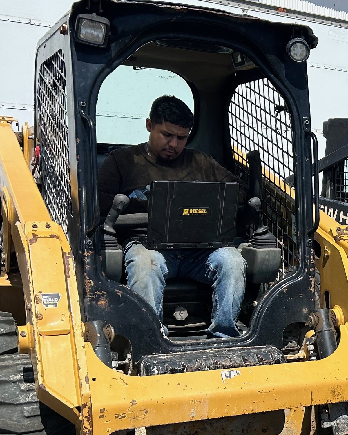Jorge, owner of Big J's Mobile Repair, seated in a skid steer running diagnostics with a diesel laptop on his lap
