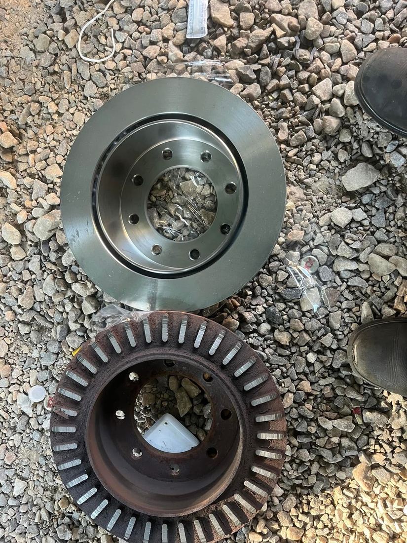 A worn brake rotor beside its new replacement, laid out on the ground at a job site