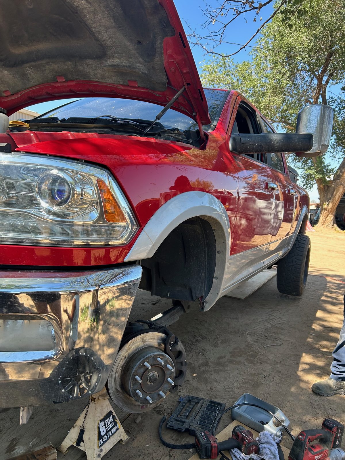 Red RAM heavy-duty pickup on jack stands with the front wheel off, exposing the brake rotor and hub during an on-site repair